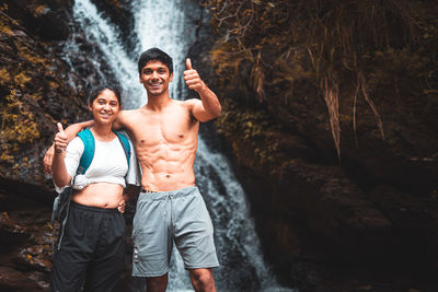 Young couple enjoying the beautiful waterfall view and showing thumbs up in the camera.