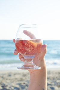 Midsection of woman holding drink at beach against sky