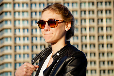 Side view of young woman in sunglasses standing by building in city