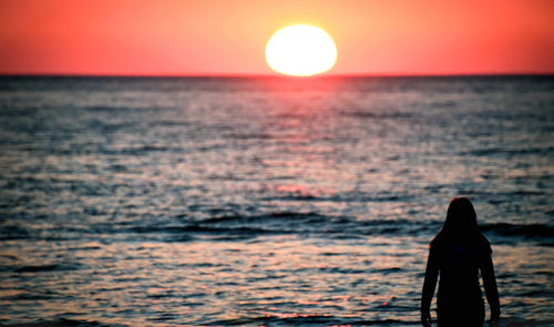 Silhouette of a young woman standing on the seashore and looking at a beautiful sunset.