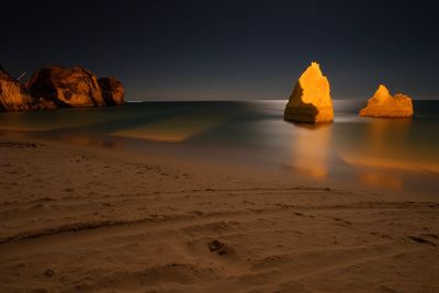 Rock formations on beach against sky during sunset