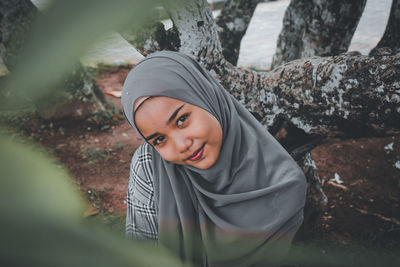 Portrait of smiling young woman against tree trunk