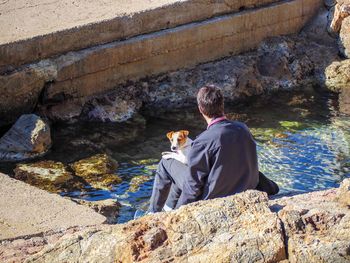 Rear view of man with dog sitting on rock