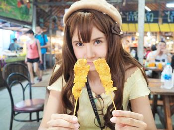 Portrait of woman holding food while sitting at sidewalk cafe