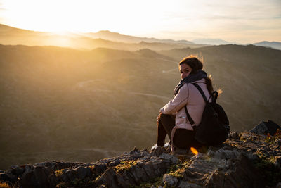 Young woman sitting on rock against mountain during sunset