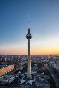 Communications tower in city against sky during sunset