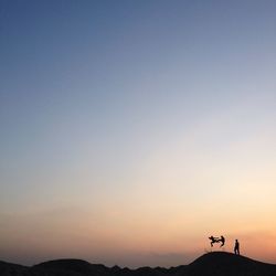 Silhouette people jumping on hill against sky during sunset