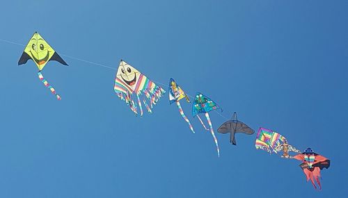 Low angle view of kites against clear blue sky