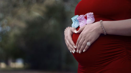 Midsection of pregnant woman with baby booties and hands on stomach standing outdoors