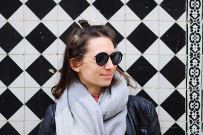 Smiling beautiful woman wearing sunglasses against patterned tiled wall