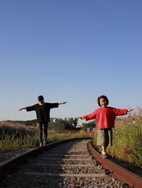Full length of mother and daughter walking on railroad tracks against clear sky