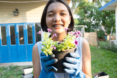 Portrait of smiling woman holding potted plant while standing in yard