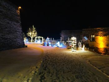 Illuminated street by buildings in city at night