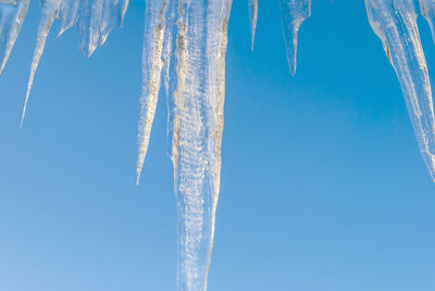 Low angle view of icicles against clear blue sky