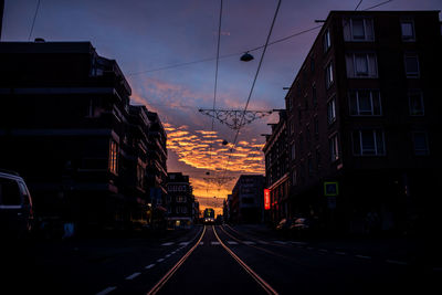 Road amidst buildings in city at sunset