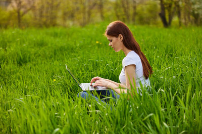 Side view of young woman sitting on grassy field