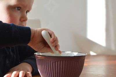 Close-up of boy with spoon in bowl on table at home