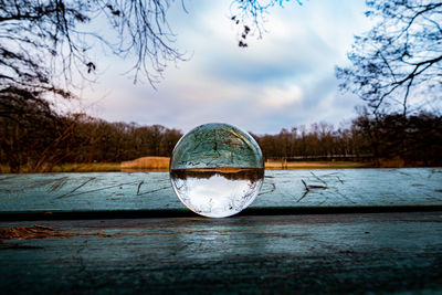 Close-up of crystal ball on glass against calm lake