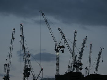 Low angle view of cranes at construction site against cloudy sky