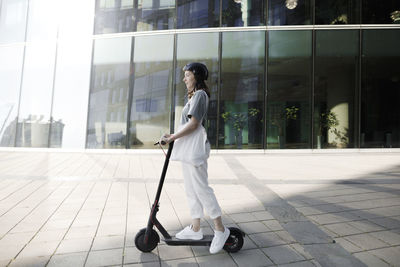 Woman with e-scooter and helmet, modern office buildings in the background