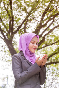 Smiling young woman praying while sitting in park