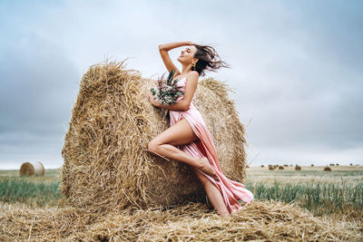 Woman standing near hay bales in field against sky