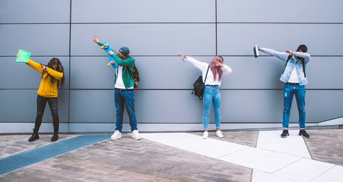 Friends posing while standing against wall in city