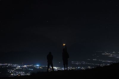 Silhouette people standing on illuminated city against sky at night