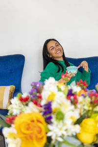 Smiling woman holding cup while sitting on sofa