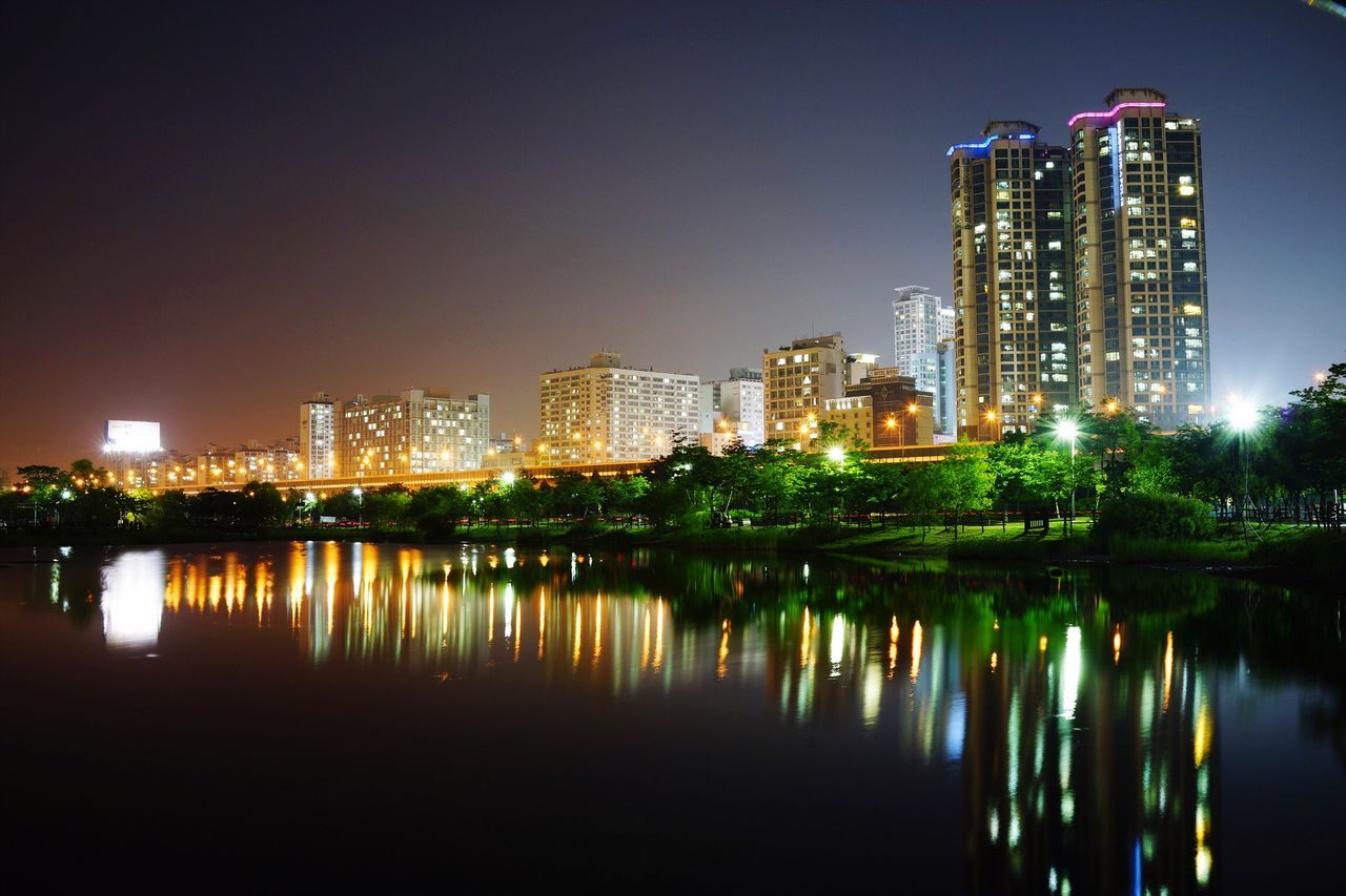 architecture, building exterior, built structure, illuminated, water, reflection, city, night, waterfront, clear sky, river, skyscraper, cityscape, tower, copy space, tall - high, urban skyline, modern, tree, lake