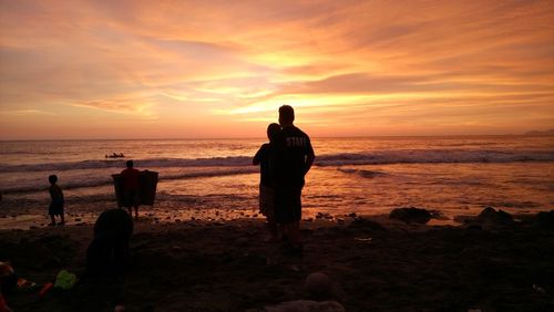 Silhouette people standing on beach against sky during sunset