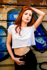 Portrait of beautiful young woman standing against graffiti wall