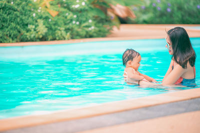 Smiling mother with son sitting by swimming pool