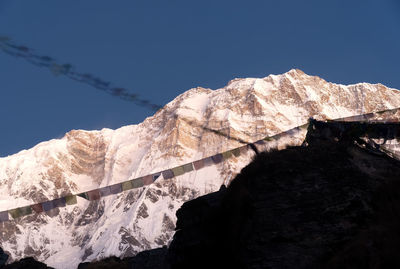 Low angle view of snowcapped mountains against clear blue sky