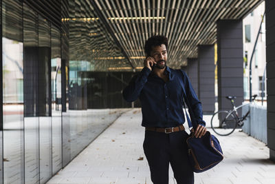 Contemplating entrepreneur with bag talking on smart phone in city