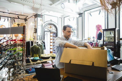 Owner unpacking cardboard box while working in clothing store