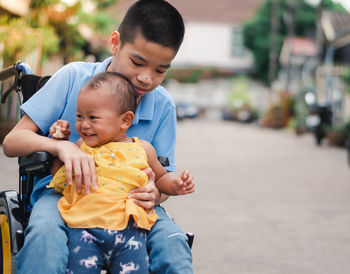 Disable boy holding cute sister while sitting on wheelchair