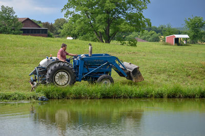 Side view of farmer with tractor working on field by lake