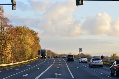 Vehicles on road against cloudy sky