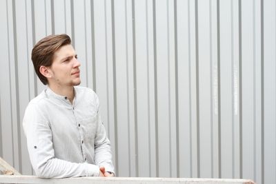 Young man looking away while standing against wall