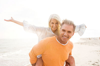 Happy man giving piggyback ride to happy girlfriend standing at beach