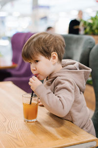 Little boy child drinks juice from a straw while sitting at a table in a cafe