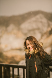 Portrait of smiling woman standing against railing in winter