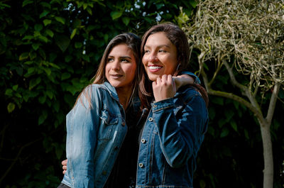 Smiling female friends standing against plants in park