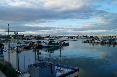 Boats moored at harbor against sky in city