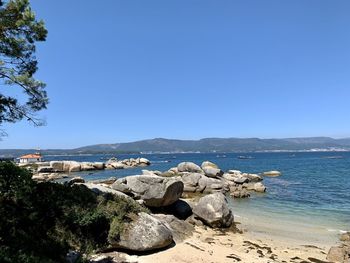 Rocks by sea against clear blue sky