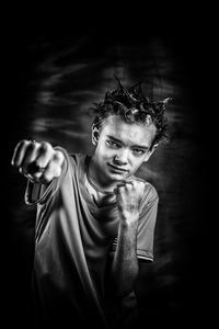 Portrait of teenage boy punching against black background