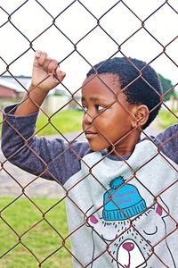 Portrait of boy seen through chainlink fence