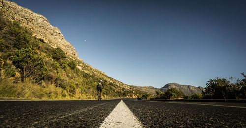 Rear view of man cycling on road against clear sky