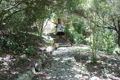 Full length portrait of happy woman jumping over footpath in forest